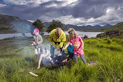 children cooking on a fire with a loch side background