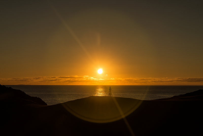 cyclist in the distance watching the sun set over the sea