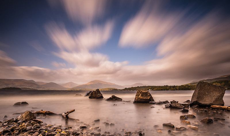 low down view of rocks by Loch Lomond clouds streaking by